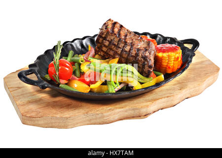 Mexican steak in cast-iron oval serving dish with handles on a wooden plate, isolated on white background. Stock Photo