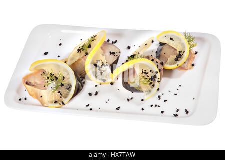 Pieces of mackerel cold smoked decorated with lemon slices on rectangular white ceramic plate, isolated on white background. Stock Photo