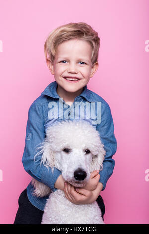 Beautiful boy with Royal Standard Poodle. Studio portrait over pink background. Concept: friendship between boy and his dog Stock Photo