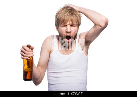 Young man with hangover holding beer bottle. Studio portrait isolated over white background Stock Photo