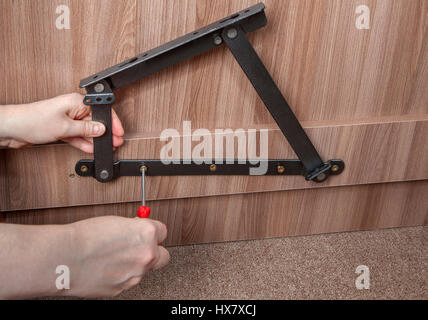 Furniture Installation, Installing steel spring bed lift system, close-up hands of installer furniture tighten screw using a screwdriver. Stock Photo