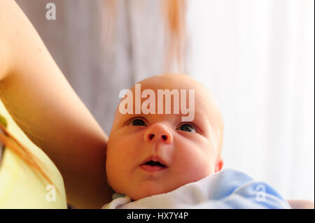 Cute baby girl makes a funny upset face on mothers hand. Stock Photo