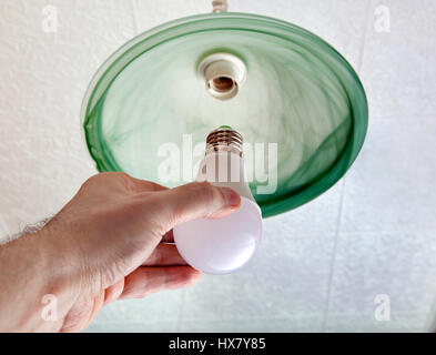 Close-up of energy-saving LED light bulb in the human hand, the replacement of the lamp in the ceiling luminaire made of green ground glass. Stock Photo