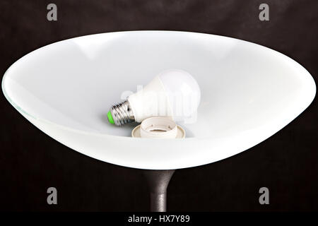 Energy-efficient LED low-energy light bulb is in the a plafond white frosted glass floor lamp, close-up shot on a dark background. Stock Photo