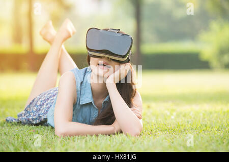 beautiful asian woman experience virtual reality sitting on grass in outdoor park. VR headset glasses device. nature outdoors background. people and t Stock Photo
