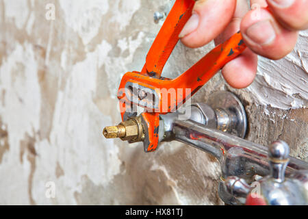 Plumber fixing water tap with leaking water users red plumber pliers. Stock Photo