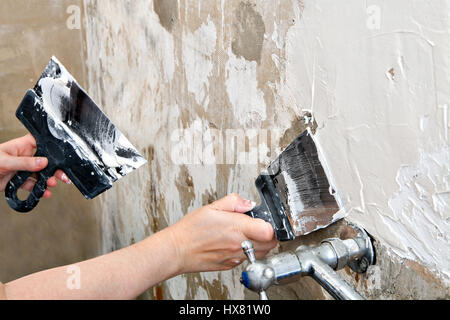 Aligning wall a painters putty, painter hands holding stainless steel spatulas, close-up. Stock Photo