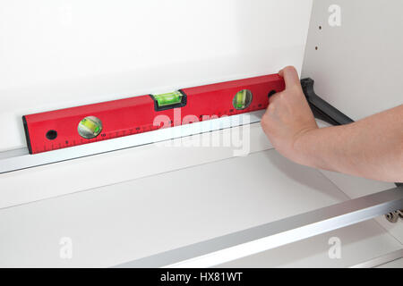 The assembly of kitchen furniture, carpenter measuring the level with special tool, close-up of worker hands holding red building level. Stock Photo