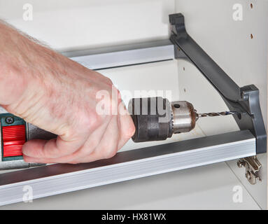 The assembly of kitchen furniture, carpenter hole is drilled using power drill, an artisan hand held an electric drill closeup. Stock Photo