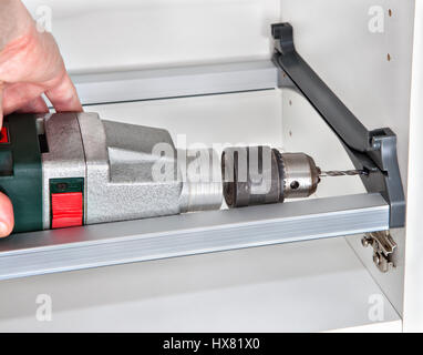Installing of kitchen furniture, cabinet wall mount assembly for drying dishes, the carpenter hole is drilled using power drill, the craftsman hands h Stock Photo