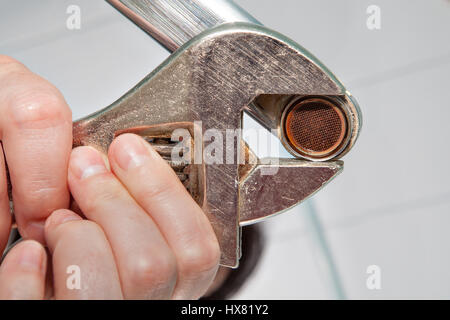 Remove the old aerator from the faucet with an adjustable wrench, close-up. Stock Photo