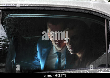Two newlyweds sitting in the car, in the passenger seat and look out the window with raindrops on glass. Stock Photo