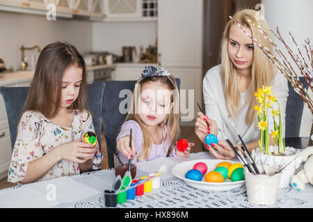 Young mother and her two daughters painting Easter eggs. Cozy home atmosphere. Easter Stock Photo