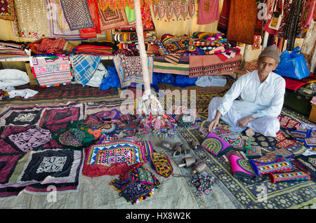 KUTCH, GUJARAT, INDIA - DECEMBER 27, 2016: An unidentified handicraft vendor in his traditional street shop selling colourful embroidery items. Stock Photo