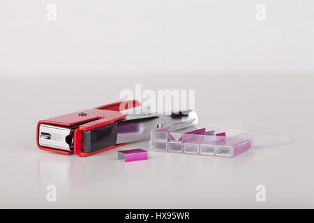Red stapler with pink staples on a white surface. Stapler and staples isolated on white background. Stock Photo