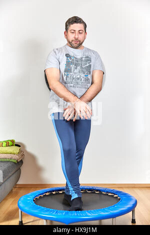 Caucasian man doing fitness exercises at home on trampoline Stock Photo