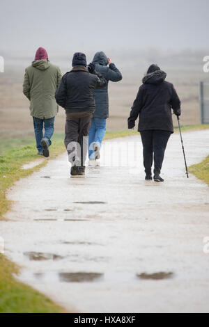 Visitors to Talacre beach in Flintshire, North Wales brave the wet and windy weather as they walk along the coastal path Stock Photo