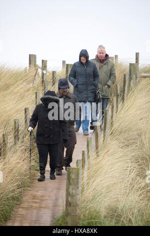 Wet and windy weather as beach visitors brave the elements walking along a path through the sand dunes at Talacre Beach in Flintshire, North Wales Stock Photo