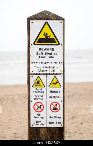 Warning sign on post in sand informing visitors to be aware of soft mud at low tide and of horses, sand yachting, no fouling, no fires, Talacre Stock Photo