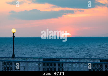 A new days sunrise on the horizon with a ship passing by over the bay at Llandudno Wales with the Victorian Pier in the foreground Stock Photo