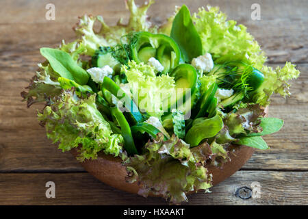 Organic mixed green vegetable salad with feta cheese and spring peas in wooden bowl close up - healthy diet organic vegan vegetarian food meal salad Stock Photo