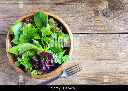 Fresh organic green mixed salad leaves over rustic wooden background - organic healthy vegan vegetarian diet detox food ingredient Stock Photo