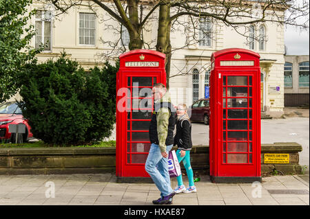 Man and young girl walking past two red old fashioned telephone boxes in Coventry, United Kingdom. Stock Photo