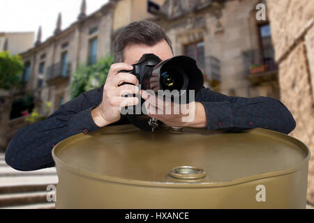 Photographer takes a picture on digital camera leaning on an iron barrel, old building on background Stock Photo