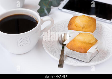 White cup with coffee, smartphone, pastry on plate, eucalyptus branch on table, business breakfast, feminine styled image for blogging, social media Stock Photo
