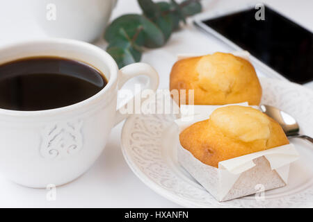 Smartphone, cup with coffee, pastry on plate, eucalyptus branch on white table, business, female blogging, styled image, top view Stock Photo