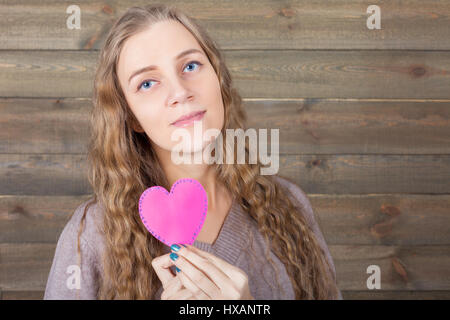 Young woman with funny pink heart in hand, wooden background. Fun photo props and accessories for shoots Stock Photo