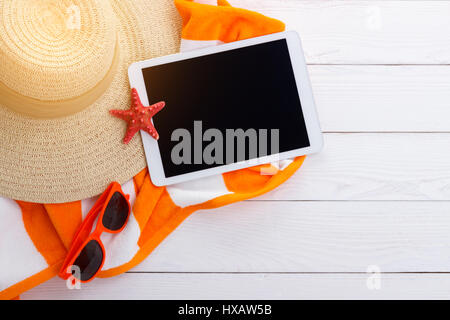 Beach accessories on wooden background for summer or vacation concept. Sunhat, sunglasses beach towel, sunburn lotion. and tablet. Space for text. Stock Photo