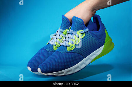 Hand holding pair of new running shoes isolated on blue background. Become sporty life Stock Photo