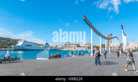 Barcelona Spain, Nov 3rd, 2013:    European Tourism.  Port Vell, large patio waterfront park,  Barefoot girls sit in sun at a bench, man plays guitar. Stock Photo