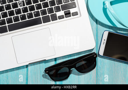 Work on the go. Modern laptop computer with smartphone and sunglasses on blue table, view from above Stock Photo