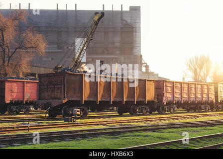 Railway station with freight wagons and train against metallurgical plant at sunset. Colorful industrial landscape. Railroad. Railway platform. Heavy  Stock Photo