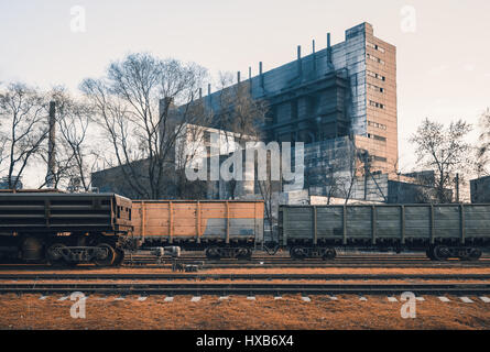 Railway station with freight wagons and train against metallurgical plant at sunset. Colorful industrial landscape. Railroad with vintage toning. Rail Stock Photo