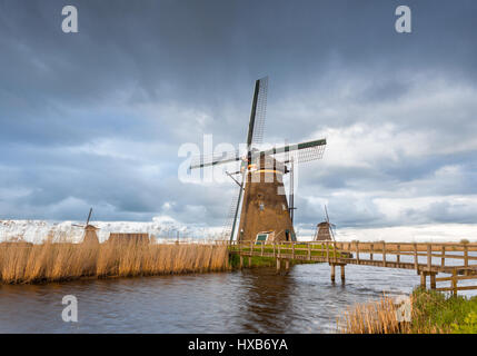 Amazing windmills. Rustic landscape with traditional dutch windmills, bridge near the water canals and blue cloudy sky. Overcast evening in Kinderdijk Stock Photo