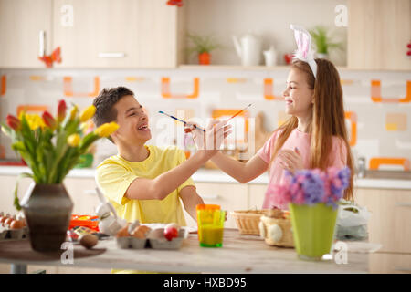 Happy male and female child in kitchen having fun while painting Easter eggs Stock Photo