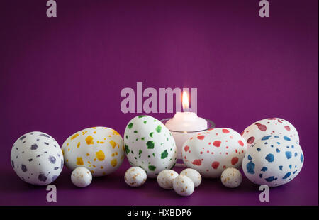 Speckled eggs, big ones and little ones with lit candle on purple background Stock Photo