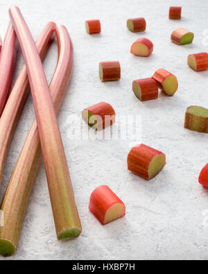 Fresh rhubarb and cut pieces of rhubarb on textured white marbled background. Shallow depth of field. Stock Photo