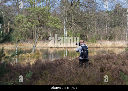 Male photographer in action with black backpack taking nature photos, seen from the back Stock Photo