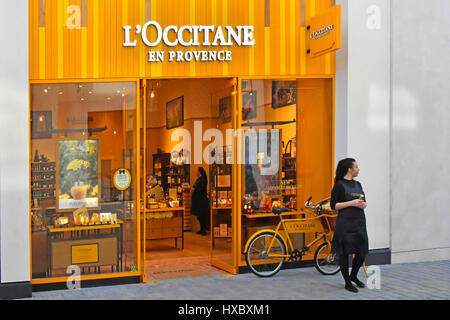 L'Occitane en Provence shop front window display of cosmetics & beauty products with sales shop assistant  person demonstrator standing on pavement Stock Photo