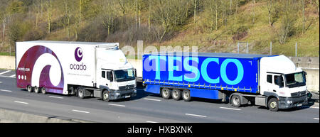 Ocado online supermarket distribution lorry overtaking Tesco supermarket store distribution truck on M25 UK motorway both with brand advertising Stock Photo