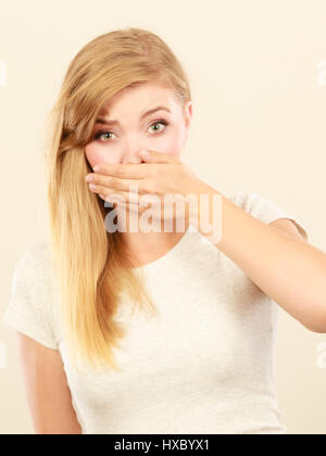 Saying bad things, shocking news concept. Ashamed young blonde woman having hand on her mouth Stock Photo