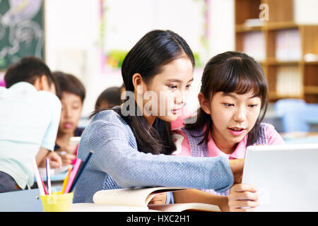 two asian elementary school girls using tablet computer while working in group. Stock Photo