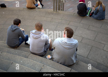 three boys enjoy junk  food lunch while sitting on the steps sauchiehall street Glasgow Stock Photo