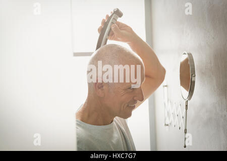 Mature man shaving head with electric razor in bathroom Stock Photo
