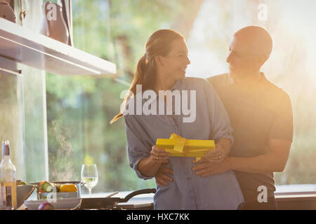 Smiling husband surprising wife with gift in sunny kitchen Stock Photo