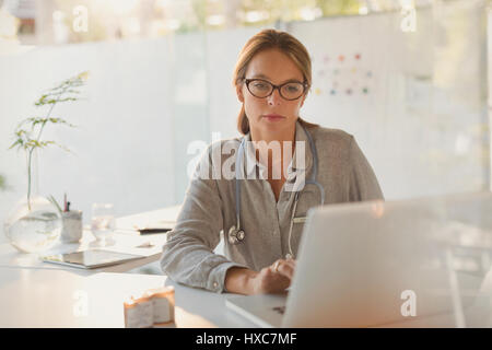 Focused female doctor working at laptop in doctor’s office Stock Photo